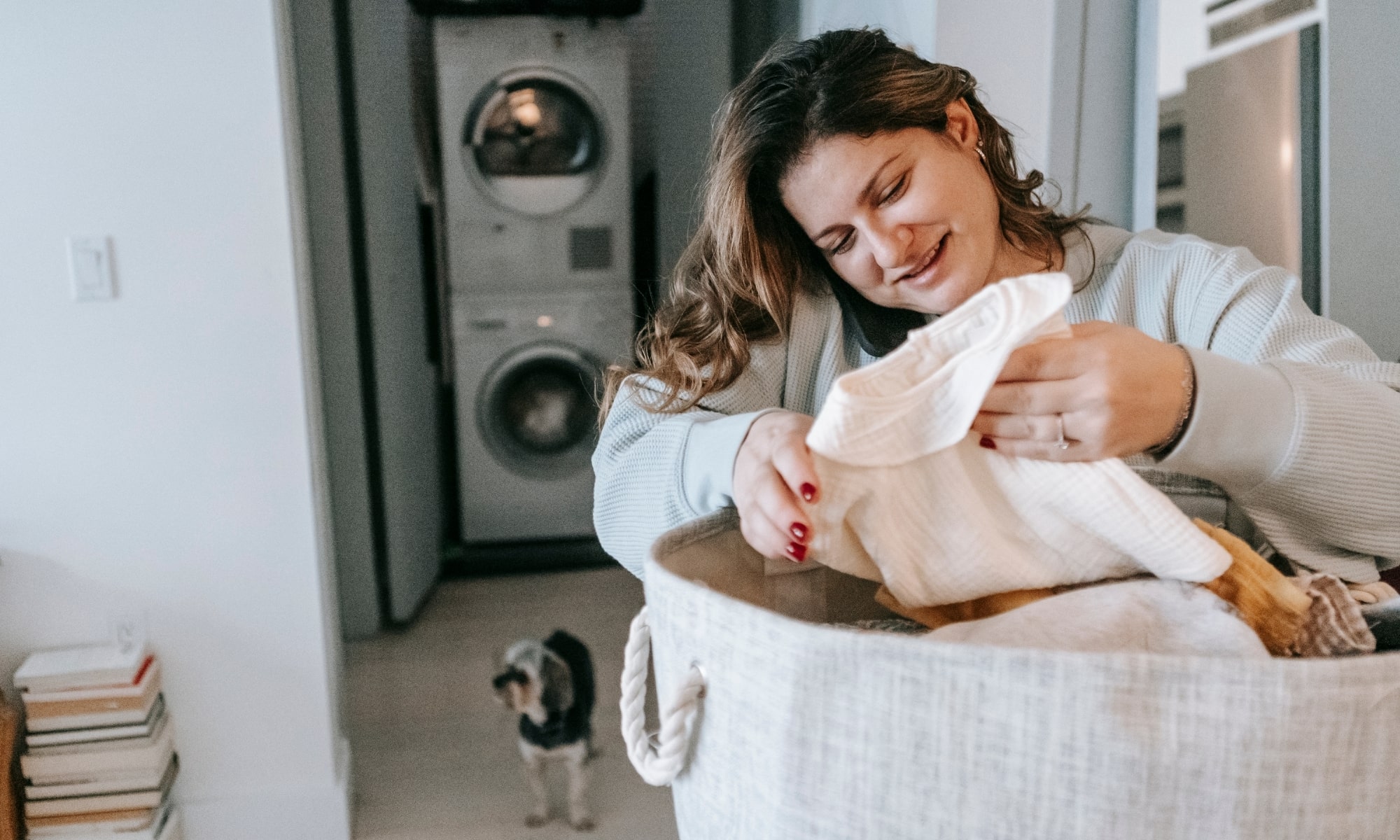 Woman smiling as she sorts laundry in her Inner West Sydney home, dog nearby and washer/dryer behind her.