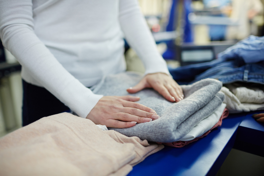 Person folding clean laundry into neat stacks on a blue table—Workwear Ready from Laundry Service Eastern Suburbs.